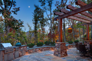 Outdoor kitchen with grill, green egg, burner, sink, and large beam pergola in a rustic style