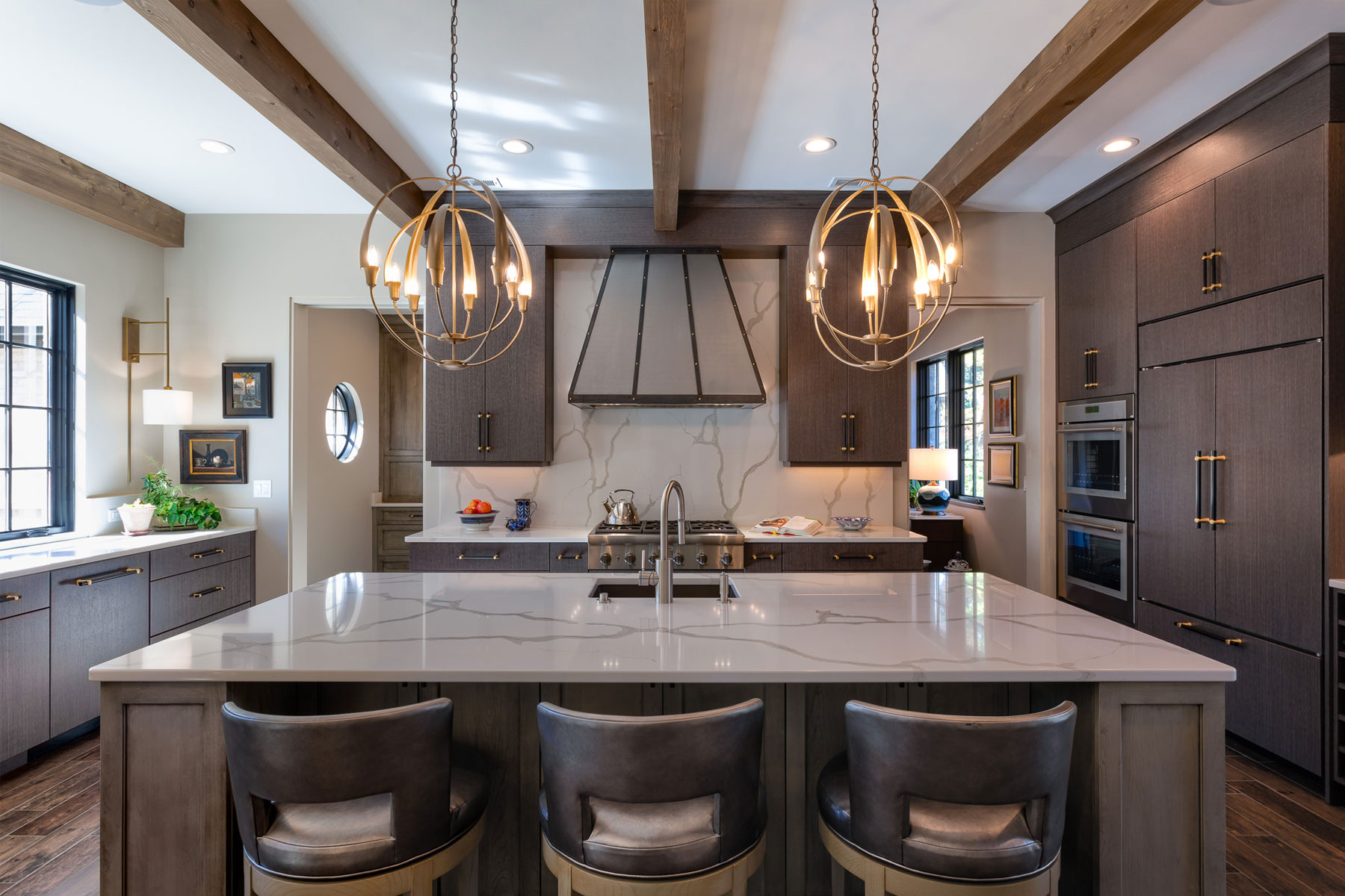 Custom range hood in kitchen with marble counters and gray cabinets