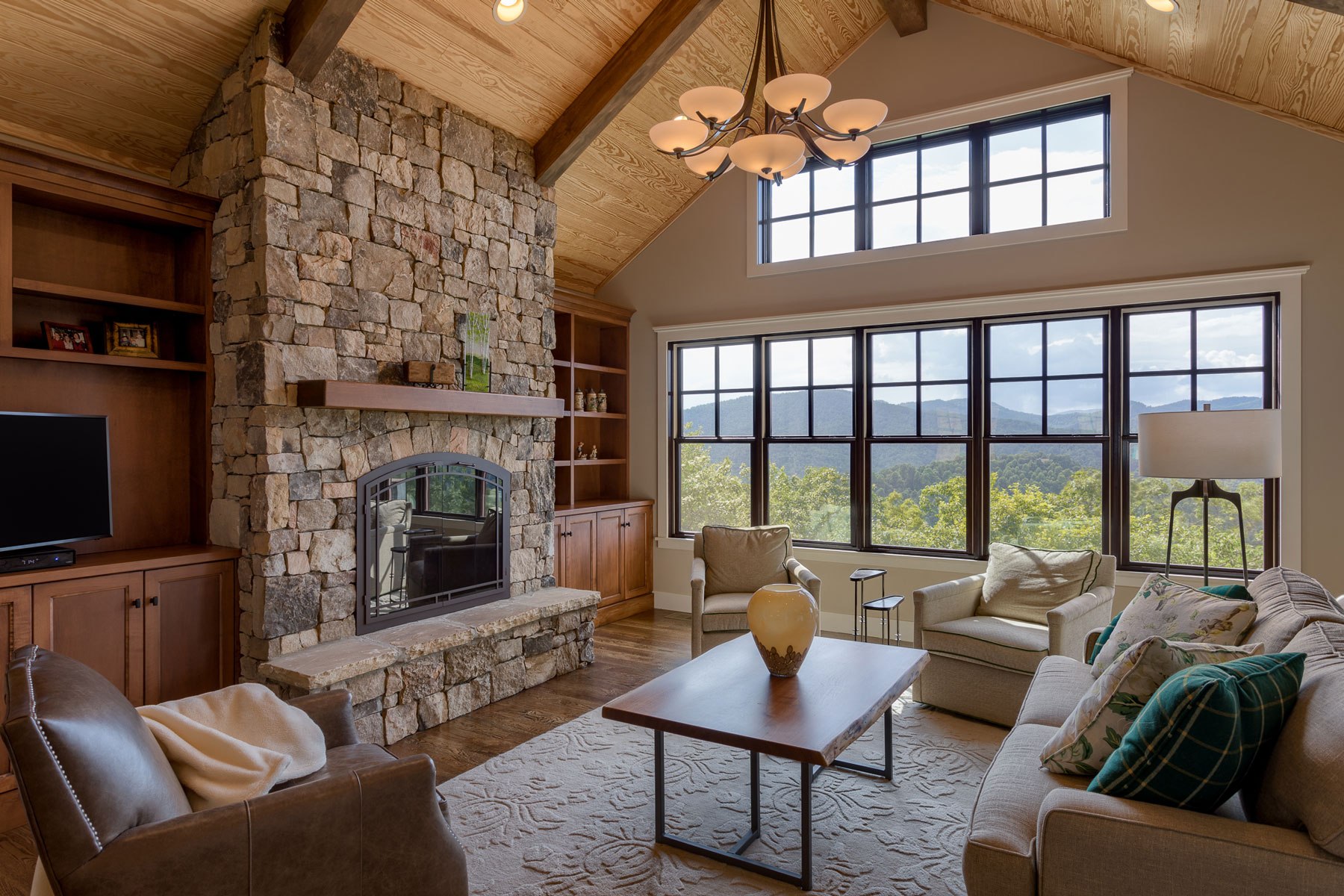 Stacked stone fireplace, builtin wood bookcases and wood clad vaulted ceiling with mountain views