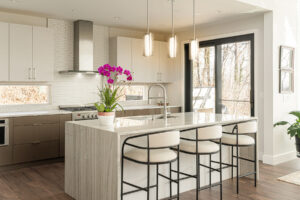 Open kitchen with clerestory windows under cabinets letting in light. Flat front cabinets with European elegance. Waterwall edge island with seating. White. cream, brown color palette kitchen.